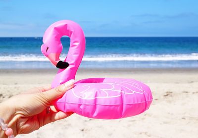 Cropped hand of woman holding flamingo shaped small inflatable ring at beach during summer