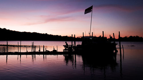 Silhouette of wooden posts in lake against sky during sunset