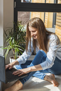 A young girl sits at home by the window at a laptop and types, writes. online communication. 