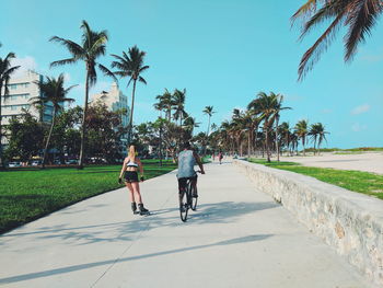 Rear view of woman inline skating by man riding bicycle on street in city