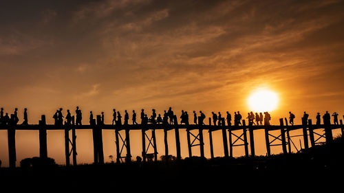 Silhouette people walking on footbridge over field against sky during sunset