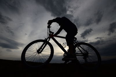 Silhouette man with bicycle against sky