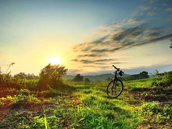 Bicycle on field against sky during sunset