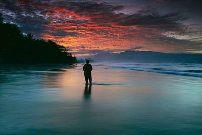 Silhouette of man standing on beach during sunset