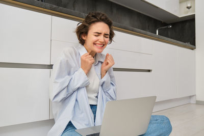 Young businesswoman using laptop while standing against wall