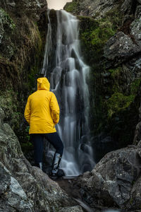 Rear view of woman standing against waterfall 