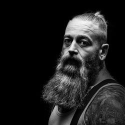 Portrait of man with beard and tattoos against black background