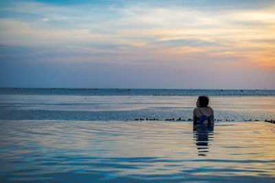 Rear view of woman in swimming pool on beach against sky during sunset