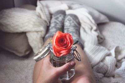 Low section of woman holding rose in glass container while sitting on bed at home