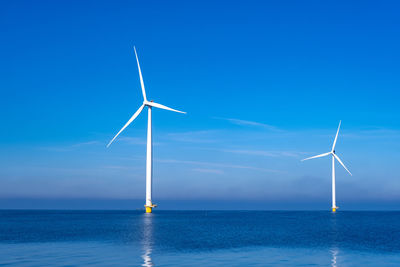 Wind turbines in sea against blue sky