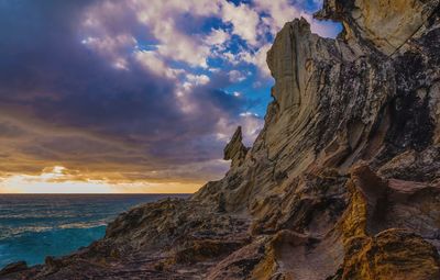 Rock formation on beach against sky during sunset