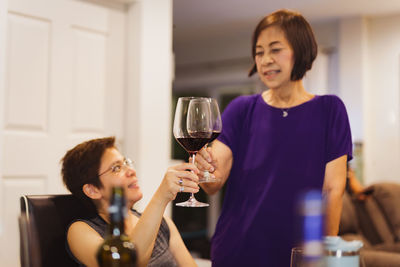 Smiling woman feeling happy while having glass of red wine with her mother.