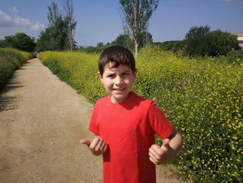 Boy gesturing thumbs up while standing on pathway by field against sky