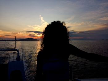 Rear view of woman at beach against sky during sunset