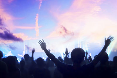 Digital composite image of crowd enjoying against cloudy sky during sunset