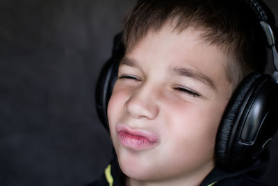 Close-up of cheerful boy listening music while making face against wall