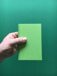 Cropped hand holding diary against green background