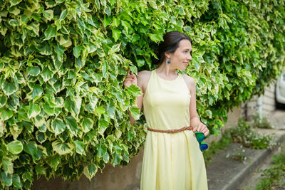 Woman staying surrounded by lush green plants, touching leaves