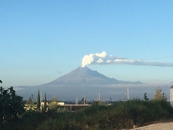 Smoke emitting from volcanic mountain against clear blue sky