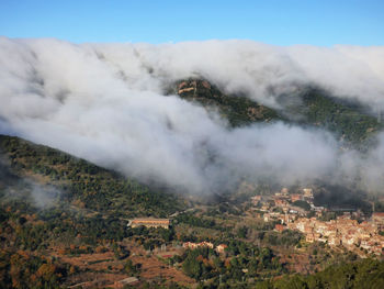 Scenic view of clouds covering mountains by village