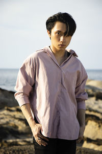 Full length of young man standing at beach against sky