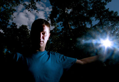 Portrait of man holding illuminated light standing against trees at night