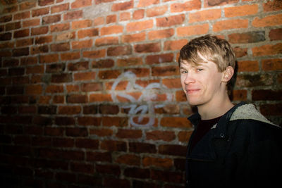 Portrait of smiling young man standing against brick wall