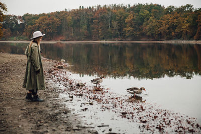 Full length of woman standing by birds and lake