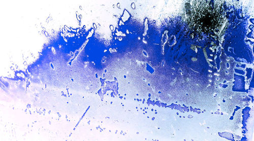 Full frame shot of wet glass window against blue background