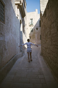 Rear view of man walking on footpath amidst buildings