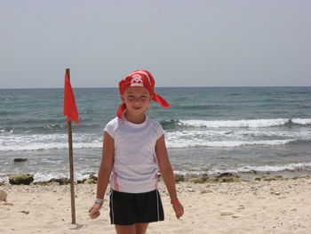 Happy girl wearing headscarf standing on sea shore at beach against clear sky