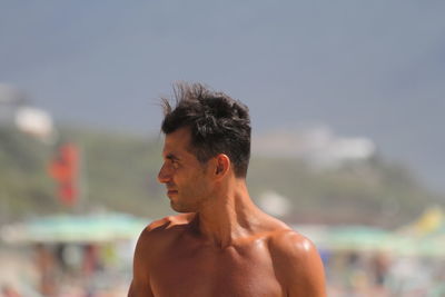 Close-up of shirtless young man standing at beach against sky