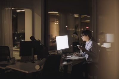 Young businesswoman with smart phone using computer at work place