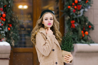 A stylish young woman walking around the city in winter, holding a potted christmas tree 