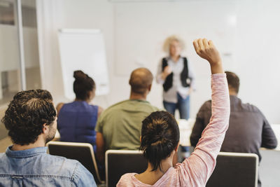 Rear view of female student sitting with hand raised in language class