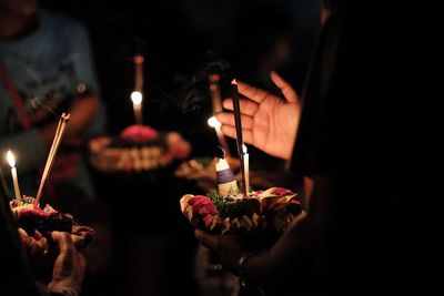 Cropped hands holding cake with candles at night