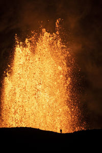 Silhouette of anonymous traveler standing against orange fume of active volcano in iceland