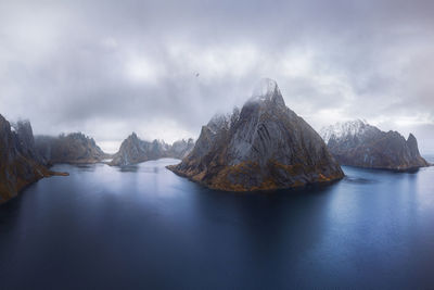 Aerial view of calm water of sea washing island with rocky formations covered in snow under cloudy sky