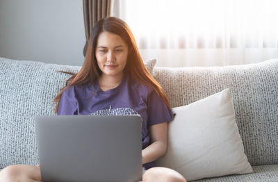 Young woman using phone while sitting on sofa at home