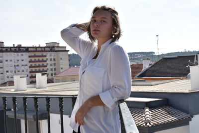 Young woman standing at balcony against sky