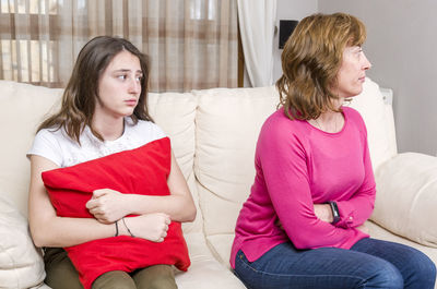 Daughter holding cushion looking at angry mother on sofa at home