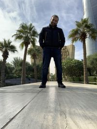 Full length of young man standing by palm trees against sky