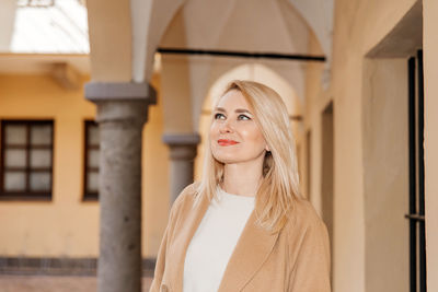 Woman with blonde hair looks up, bathed in sunlight amidst classic architecture