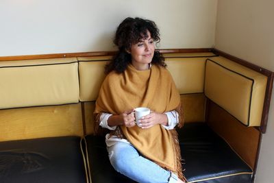 Woman holding coffee cup while sitting on sofa at home