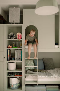 Full length portrait of boy with down syndrome sitting on bunkbed ladder at home