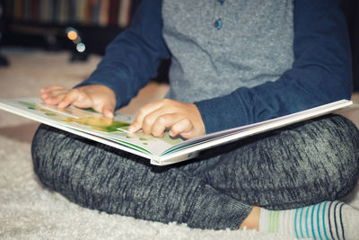 Midsection of man using mobile phone while sitting on book