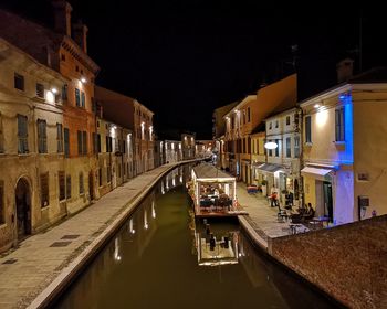 Canal amidst illuminated buildings in city at night