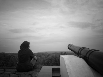 Rear view of woman looking at landscape while sitting against sky