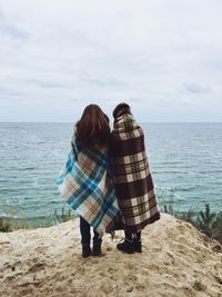 Rear view of couple standing on beach against sky