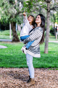 Side view of smiling mother carrying cute daughter while standing in park